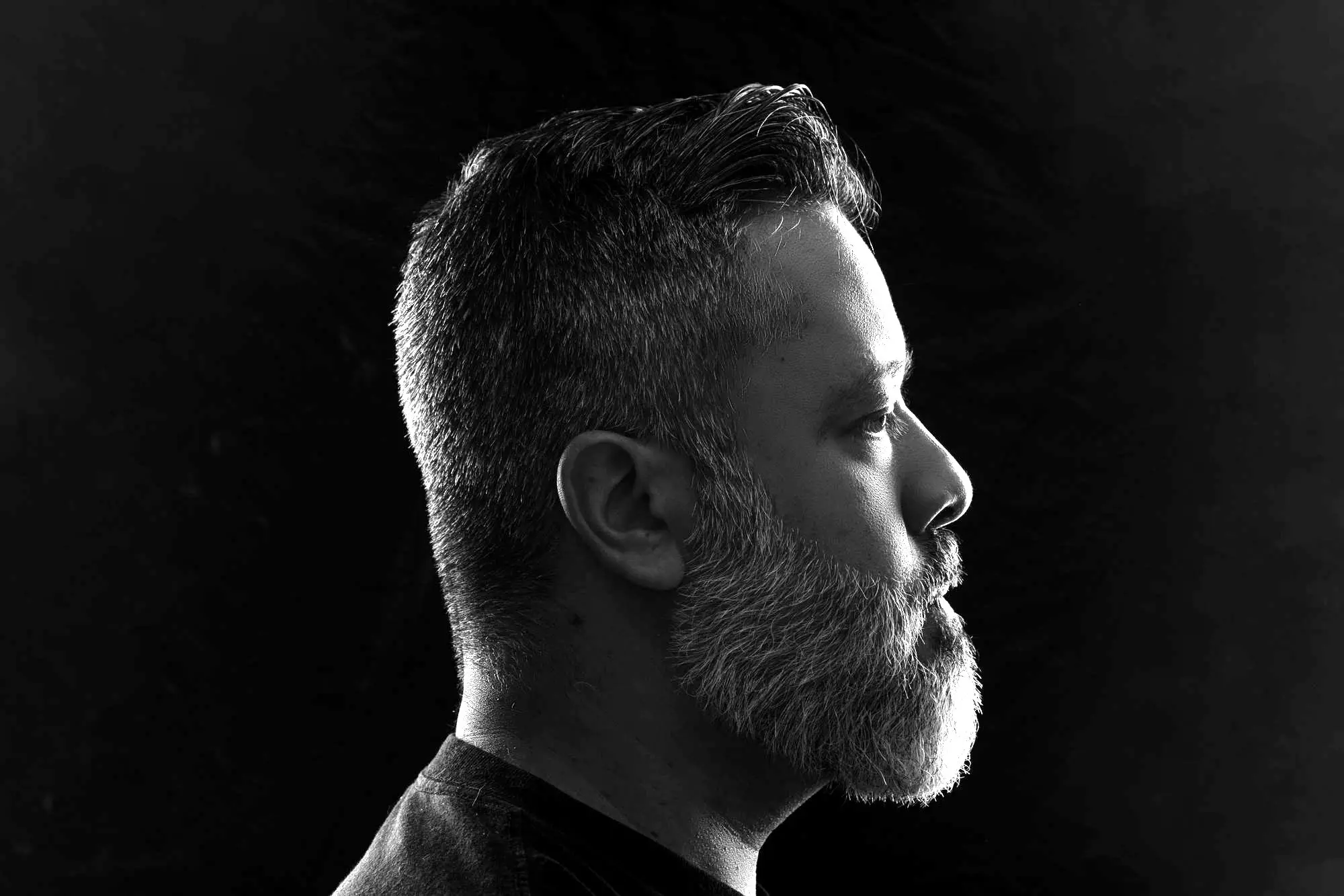 Perfil de un hombre con barba recortada en estudio oscuro